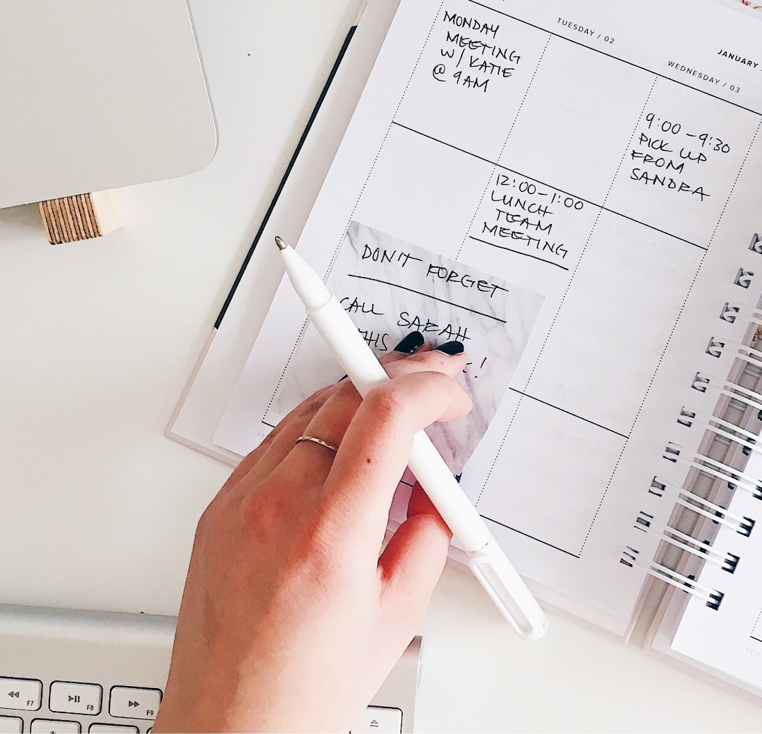 a close up of a hand holding a pen over a paper planner