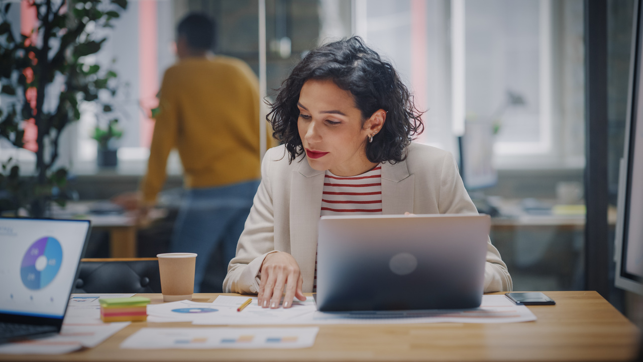 woman looking at charts on paper in front of her laptop