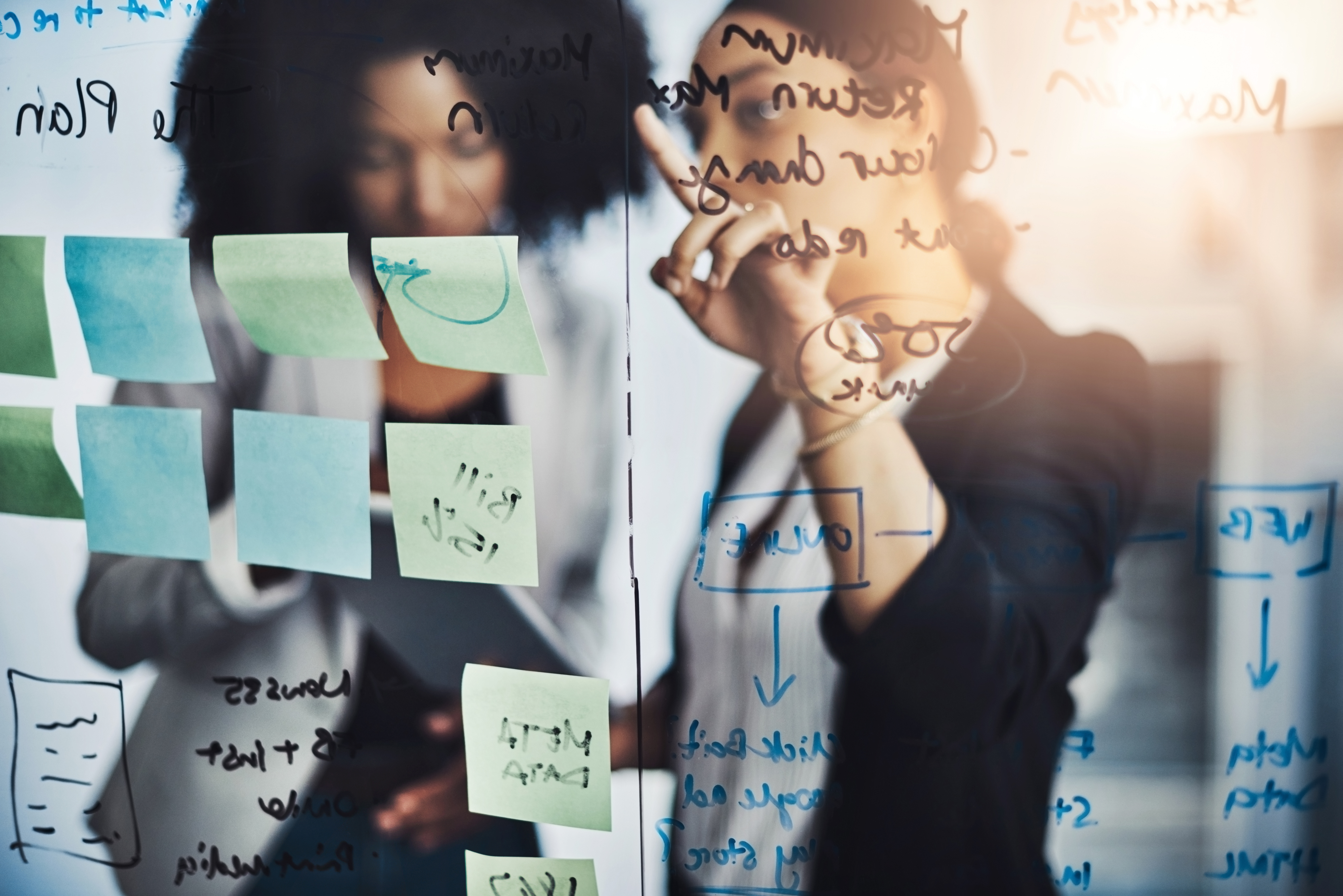 two women pointing at a whiteboard