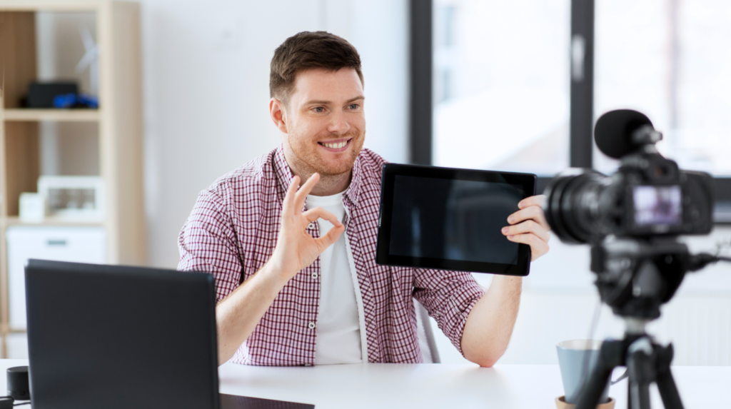 a person holding up a tablet computer while sitting at a desk in front of a camera.