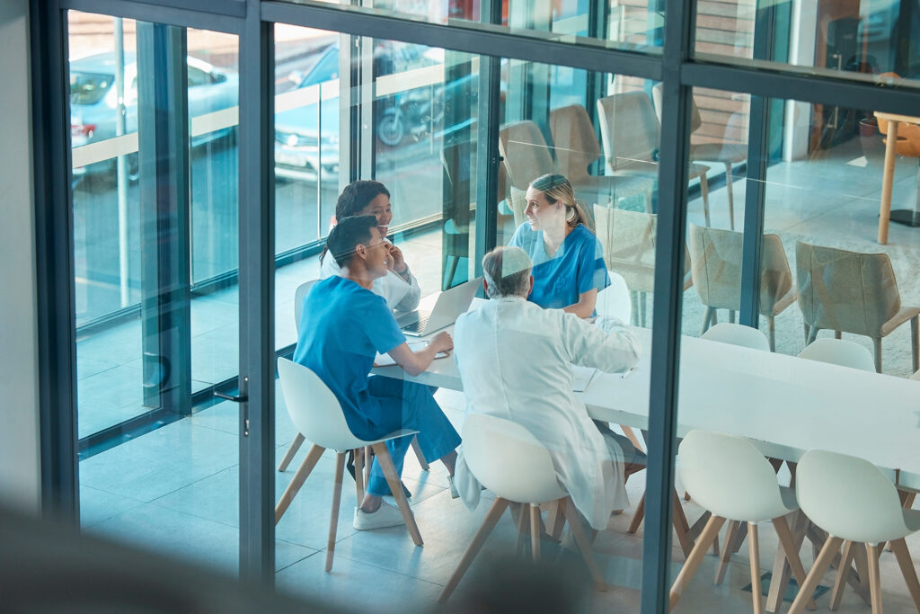 View into a meeting with four diverse medical professionals through the outside of a meeting space