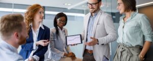 a group of business people standing around a table with a laptop