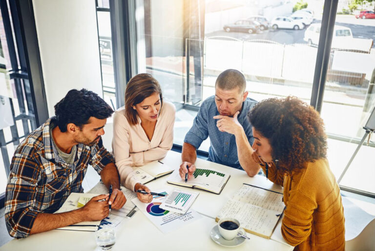 group of people sitting around a table reviewing a "land and expand" strategy chart